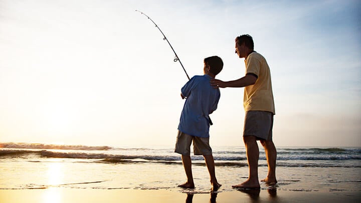 Man and boy boy fishing at sunset on a beach