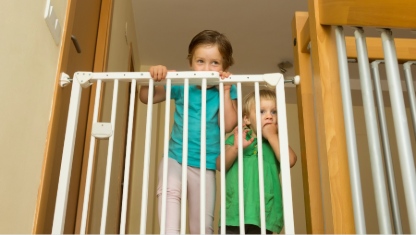 Two little girls approaching safety gate of  stairs at home