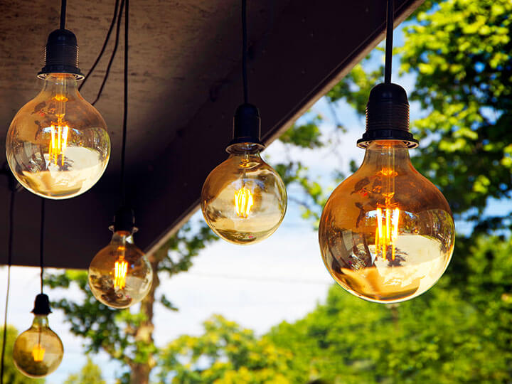 Several lit globe lightbulbs hanging from an awning with green trees in the background 