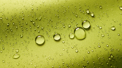 Top view closeup of green background with small round drops of water on textured waterproof impregnated fabric in light room