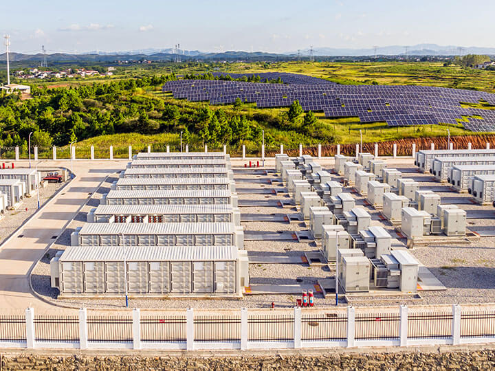 Aerial view of energy storage power station with solar panel field and trees in the background